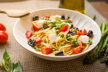 Pasta primavera spaghetti close up with cherry tomatoes, black olives, feta cheese and basil, served on wooden table, with natutal light, italian dish and cuisine homemade