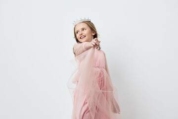 Cute girl in a pink princess dress with a crown, smiling and pointing, set against a light background, perfect for children s parties and celebrations