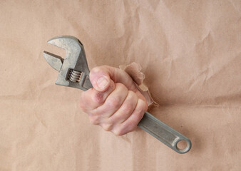 Man`s hand with adjustable wrench on craft paper background