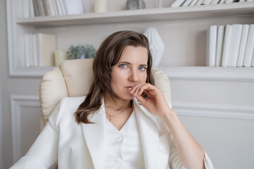 Fototapeta premium A woman, a businesswoman in a white suit, is sitting at a desk in an office, working with a laptop and a calculator. The workflow of an office worker is shown