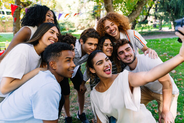 Cheerful young multi ethnic friends gathering in a park, happily taking a selfie at a lively party, capturing joyful moments together
