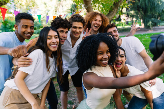Group of cheerful young multiracial people taking a selfie in a park during a party with colorful pennants
