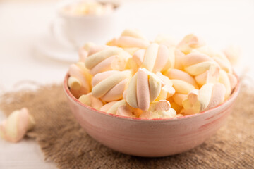 Orange and pink marshmallow in ceramic bowl on white wooden, side view, selective focus