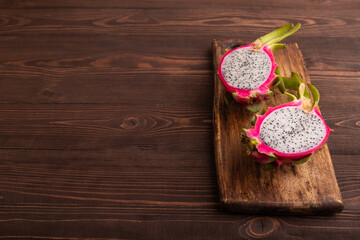Ripe Pitaya on cutting board on brown wooden background, side view, copy space