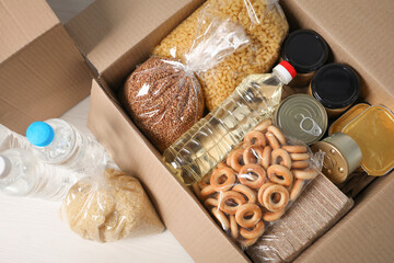 Different food products in box on light wooden table, flat lay