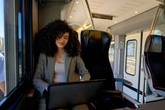 Young businesswoman working on a laptop while enjoying a comfortable train journey, highlighting the blend of modern commuting and productivity in todays professional landscape