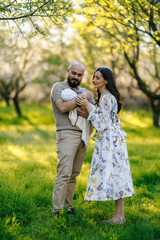 Fototapeta premium A man and a woman are gently holding a baby in a beautiful park