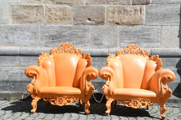zwei orangefarbene Sessel in barockem Stil, aus Plastik an öffentlichem Platz auf...