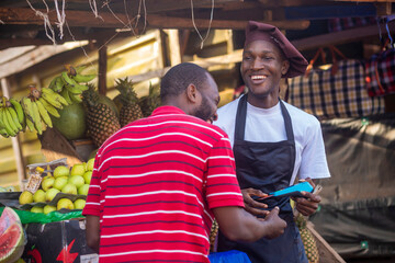 Person paying for fruits with a credit card while african fruit seller holding an electronic POS machine
