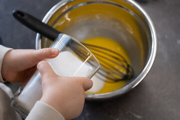 Child s small hands holding glass of sugar near egg mixture