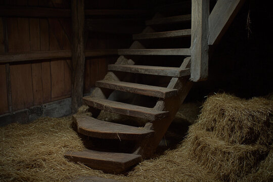 Rustic wooden staircase leads to hay loft in an old barn during the quiet of a summer afternoon