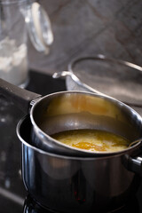 Smooth, fully melted butter in a saucepan over a double boiler setup on a black stovetop, with a spoon partially visible for stirring. Vertical image.