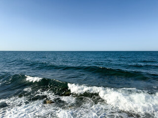 ocean waves crashing the shore under a clear blue sky. blue tones. deep blue. minimalist sea background. nature symmetry. straight