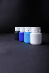 Small bottles of blue, white and black acrylic or gouache paint jars in a box on dark background....