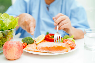 Asian elderly woman patient eating salmon stake and vegetable salad for healthy food in hospital.