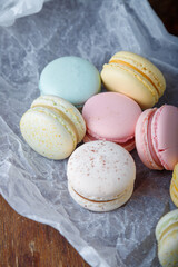 Tender multicolored macaroons with different flavors on paper, wooden rustic background. Top view, closeup shot