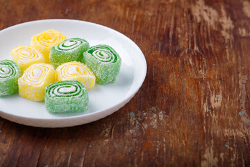 Turkish delight, yellow and green locum roll with coconut flakes on white plate, wooden background. Eastern sweets, oriental food. Traditional tasty dessert. Copy space. Top view