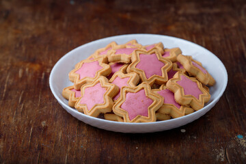Star shaped cookies with pink frosting on white plate, wooden rustic background. Strawberry icing on cookies in shape of stars. Closeup