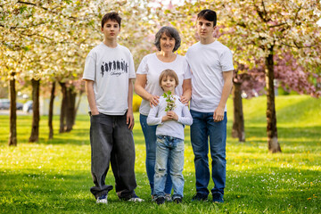 Fototapeta premium Portrait of cute stylish smiling family, boys and grandmother sitting in the grass in park