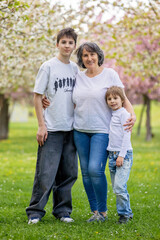 Fototapeta premium Portrait of cute stylish smiling family, boys and grandmother sitting in the grass in park