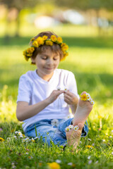 Portrait of cute stylish smiling toddler boy sitting in the grass in park