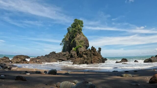Limestone karst Pyramid Rock stands in the tropical sea at Karang Agung Beach, Kebumen, Indonesia. Ocean waves surround coastal rock formation. Sunny day seascape nature view