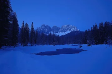 Fototapete Frozen winter landscape at dawn,  a tranquil scene of snow-covered forest, icy lake, and majestic mountain range beneath a  pale blue sky © Ibnu