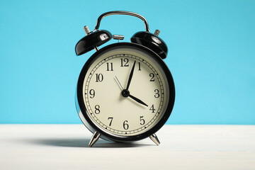 One black clock on white wooden table against light blue background