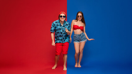 Fototapeta premium Smiling couple standing side by side in summer style expressing happiness and balance, dancing against split red and blue background. Concept of human emotions, relationship, lifestyle.