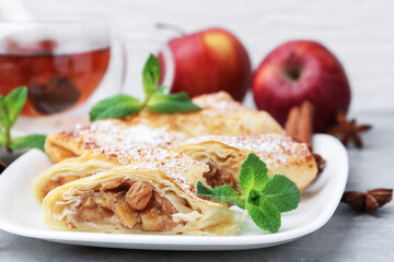 Tasty apple strudels with powdered sugar and mint on light grey table, closeup