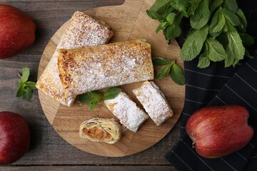 Tasty apple strudels with powdered sugar, mint and fruits on wooden table, flat lay