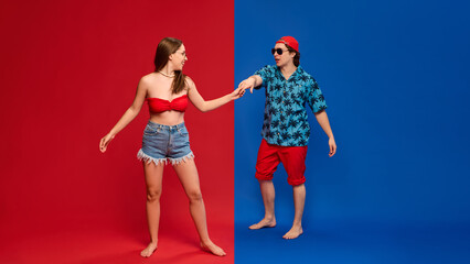 Fototapeta premium Young man and woman in summer clothes, dancing against split red and blue background. Concept of human emotions, relationship, lifestyle, happiness, summer vibe, party, celebration
