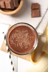 Tasty chocolate milk in glass, banana and pieces on white wooden table, flat lay