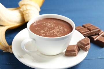 Tasty chocolate milk in cup, pieces and banana on blue wooden table, closeup