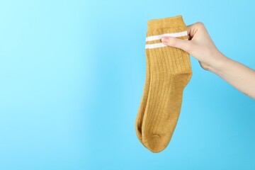 Woman with pair of socks on light blue background, closeup. Space for text
