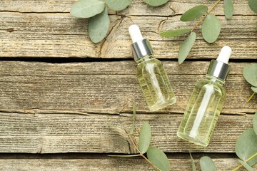 Bottles of essential oil and eucalyptus leaves on wooden table, flat lay. Space for text © New Africa