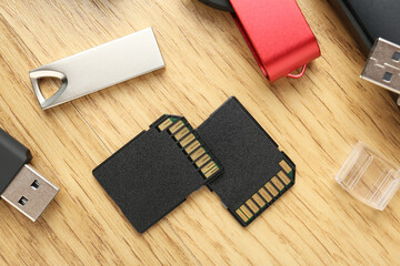 Flash drives and SD memory cards on wooden background, flat lay
