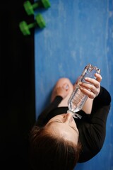 girl drinks water. woman replenishes water balance after a workout while sitting on a mat. healthy...