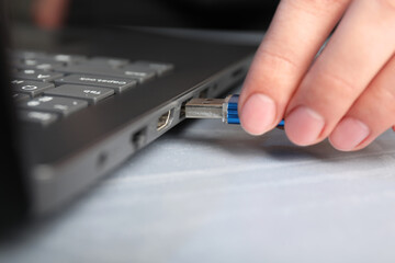 Woman inserting flash drive into laptop at gray table, closeup