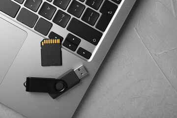 Modern flash drive, SD memory card and laptop on light grey table, flat lay. Space for text