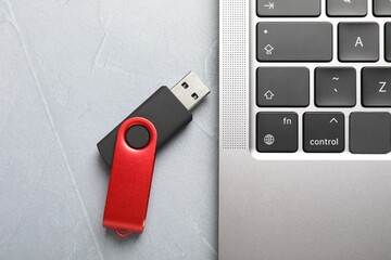 Modern flash drive and laptop on light grey table, flat lay