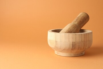 Wooden mortar and pestle on light brown background, closeup. Space for text