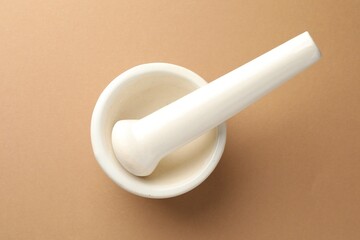 Ceramic mortar and pestle on light brown background, top view