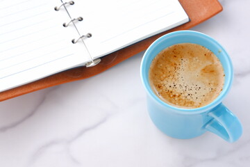 ミルクをたっぷり入れたコーヒー、カフェ・ラッテを飲みながら、システム手帳でデスクワークをしているイメージの写真素材
