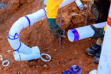 Construction workers are fitting PVC pipes together in trench, ensuring secure connection for...