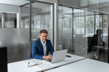 Smiling senior businessman entrepreneur sitting at desk working on financial project, looking thinking at screen. Mature 50s Latin business man ceo manager using laptop computer in office. Copy space