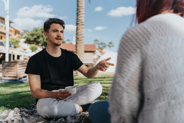 A peaceful interaction between two individuals seated on the ground under a sunny sky in a park...