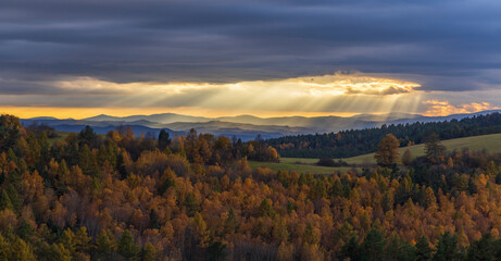 Sun rays shining through clouds over colorful autumn forest landscape with Low Tatras