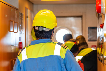 Crew members in blue coveralls and yellow helmets seen from behind during a safety drill on a...