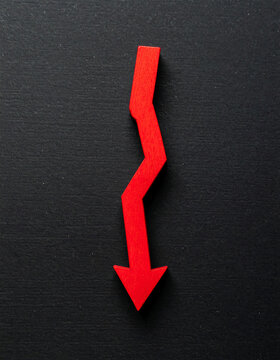 Red wooden arrow pointing down on black background. Business, market decline or economic.
